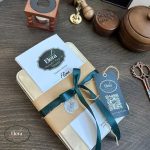 تصویر بسته بندی کیت گلدوزی به وقت اصالت که یک جعبه ی فلزی با کاغذ کرافت و ربان سبز هستش با یه مهر مومی الرا بسته بندی بسیار شکیل و زیبا برای یک هدیه ی ماندگار عاشقانه و یادگاری شیک و تعاملی با هنر